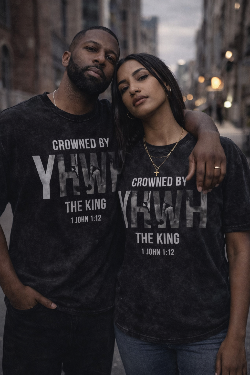 Two people wearing black t-shirts with 'Crowned by YHWH, The King 1 John 1:12' text on a city street.